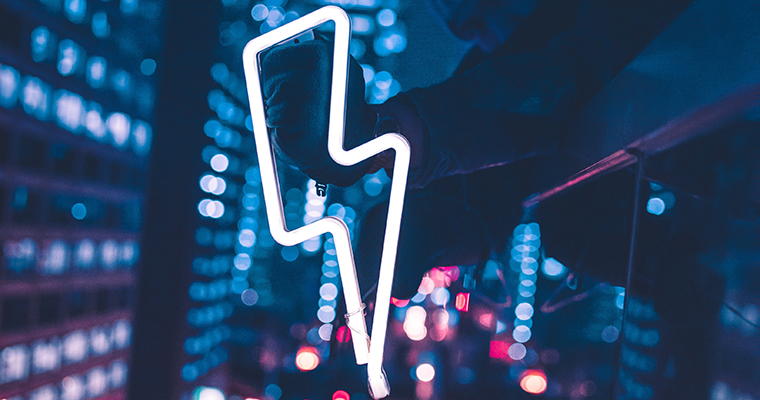 En kille som lutar sig ut från en byggnad och håller i en elkraftsymbol i neon. I bakgrunden syns en storstad.